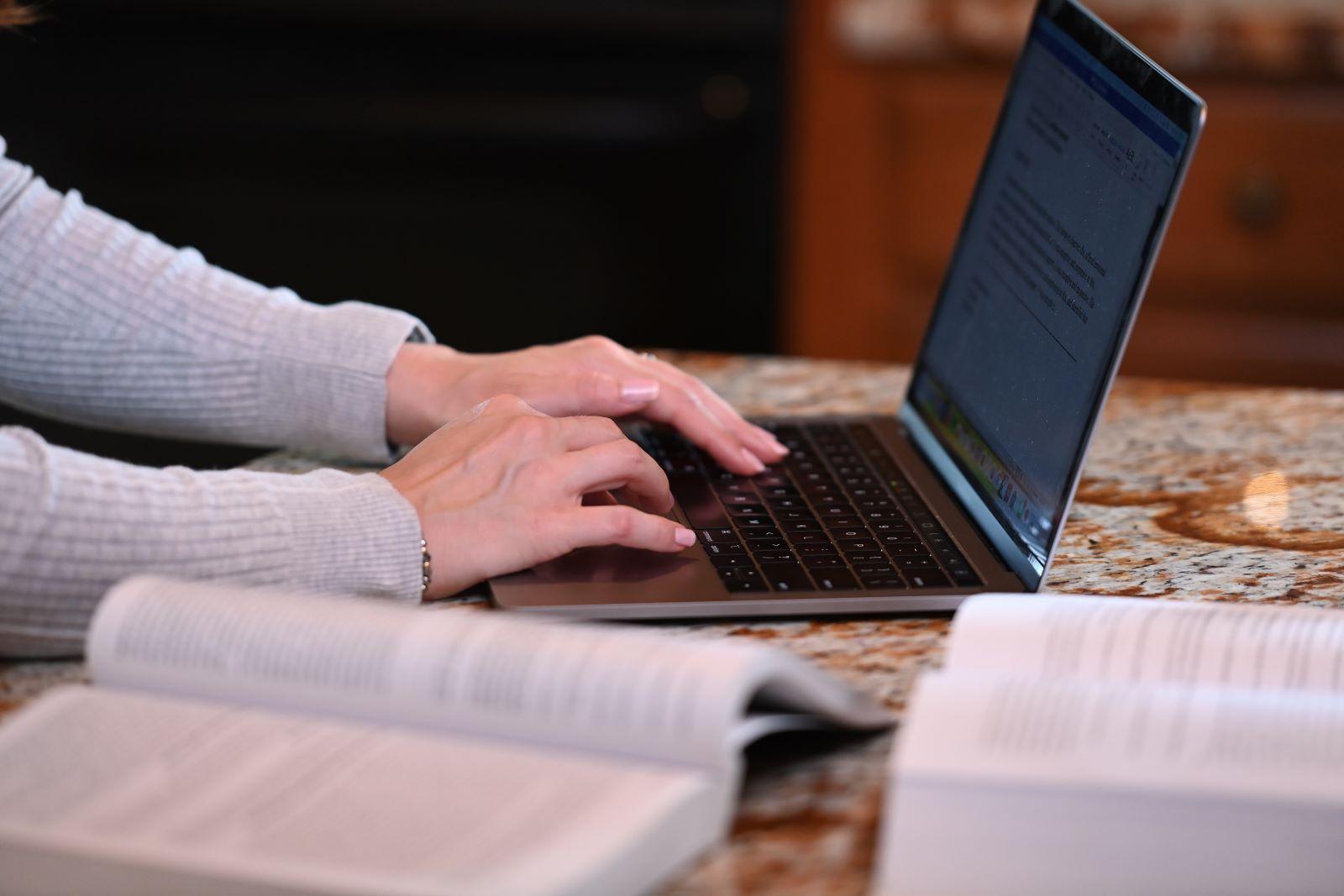 Counseling student typing on laptop with books open on the counter