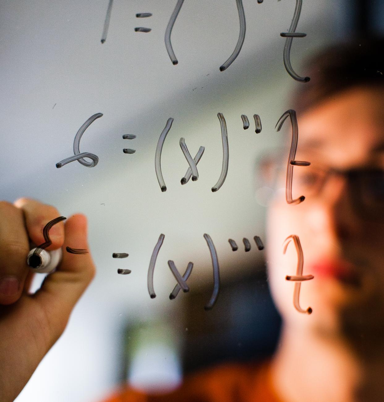 Student writing math equations on a window