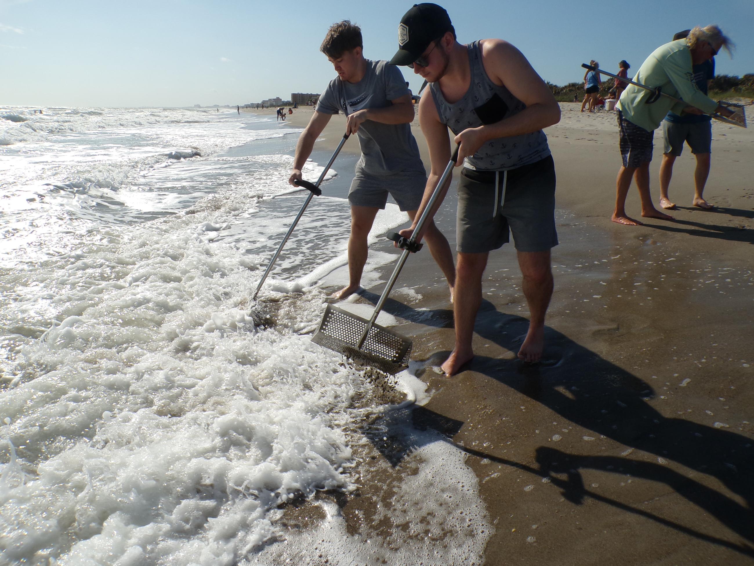 Two Waynesburg students use a scooping shovel to dig through the sand