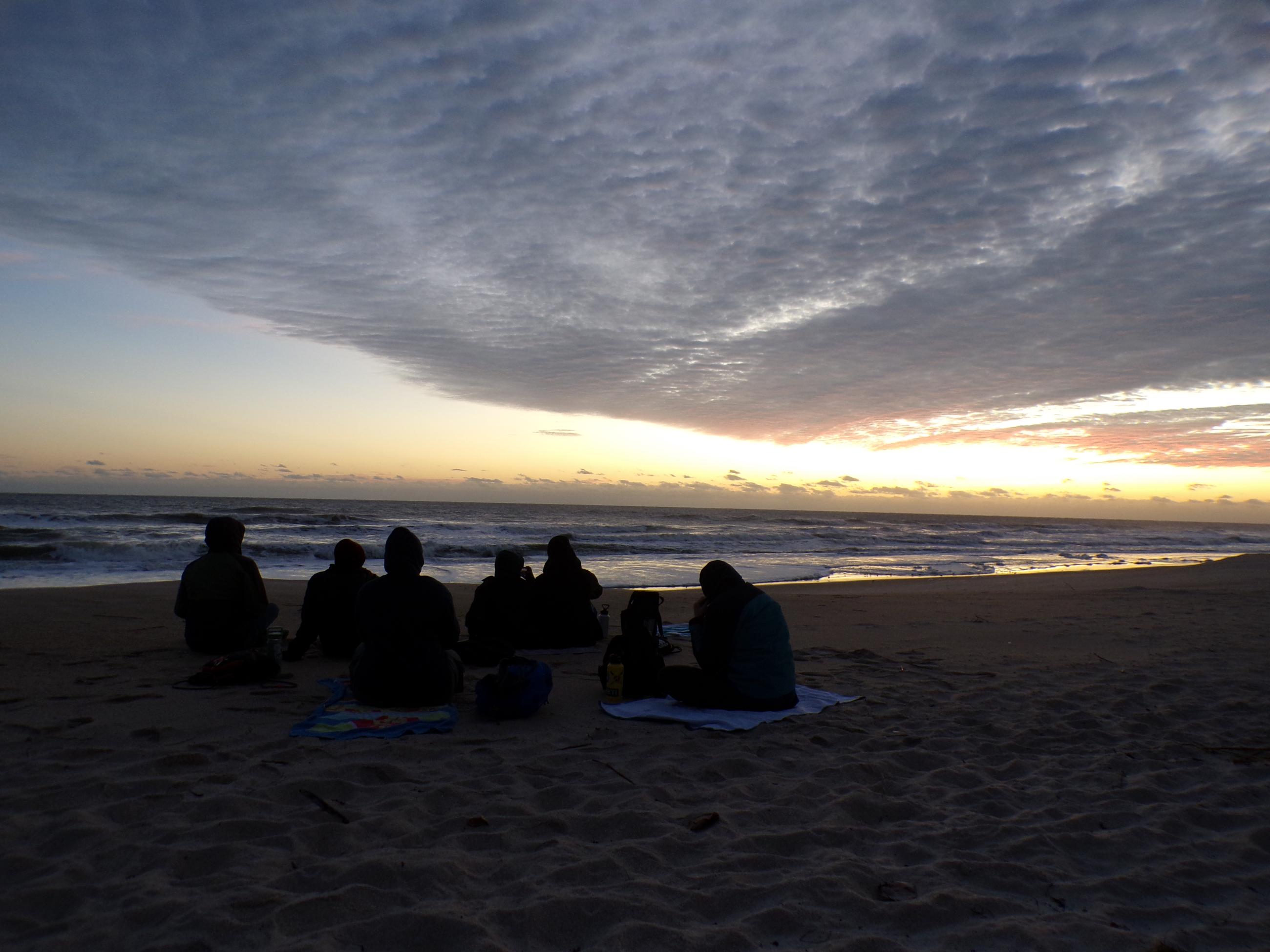 Participants sit on the beach as they watch a beautiful sunset across the ocean