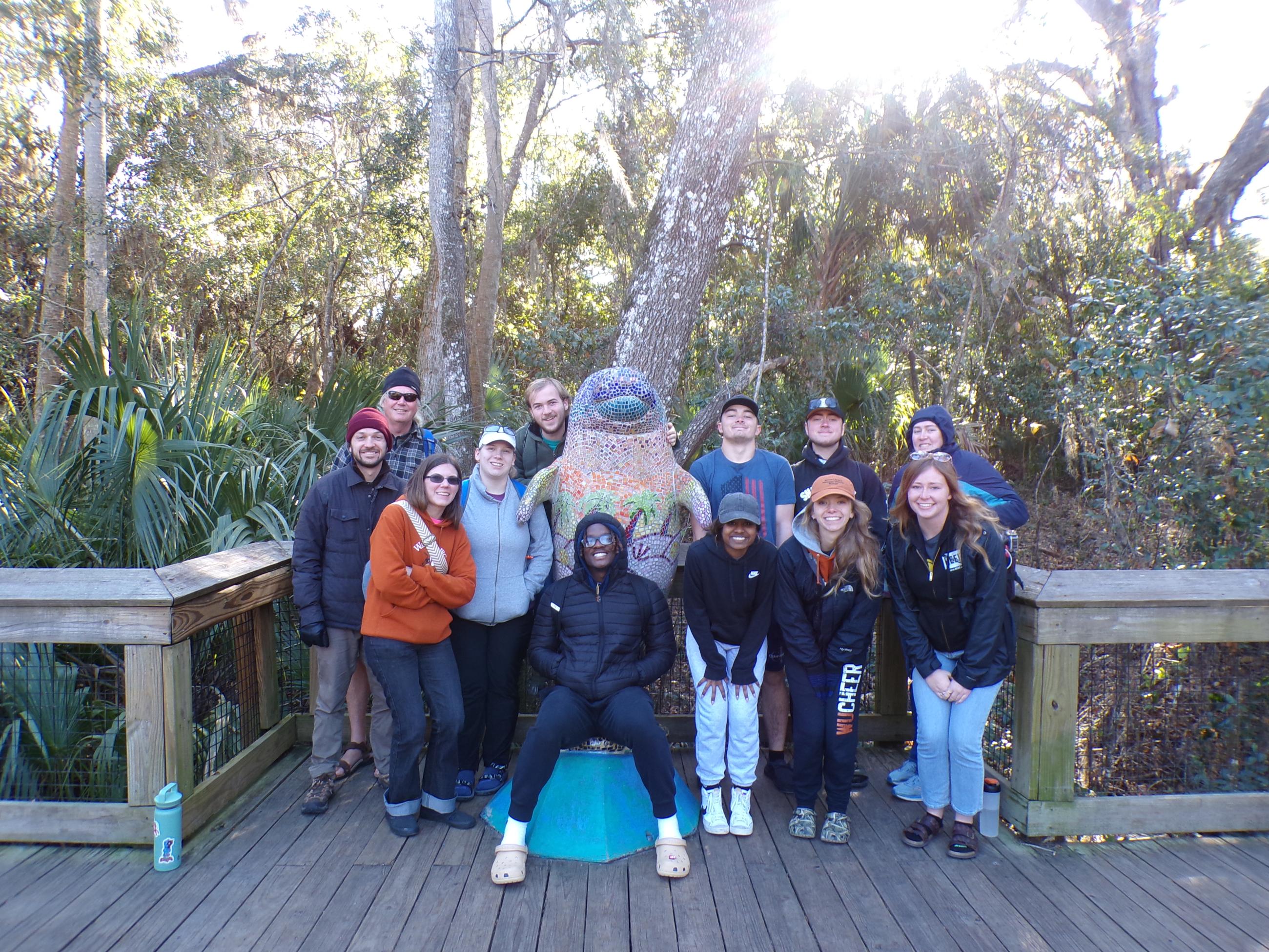 The group gathers around a colorful dolphin statue with an expanse of Florida wildlife behind them