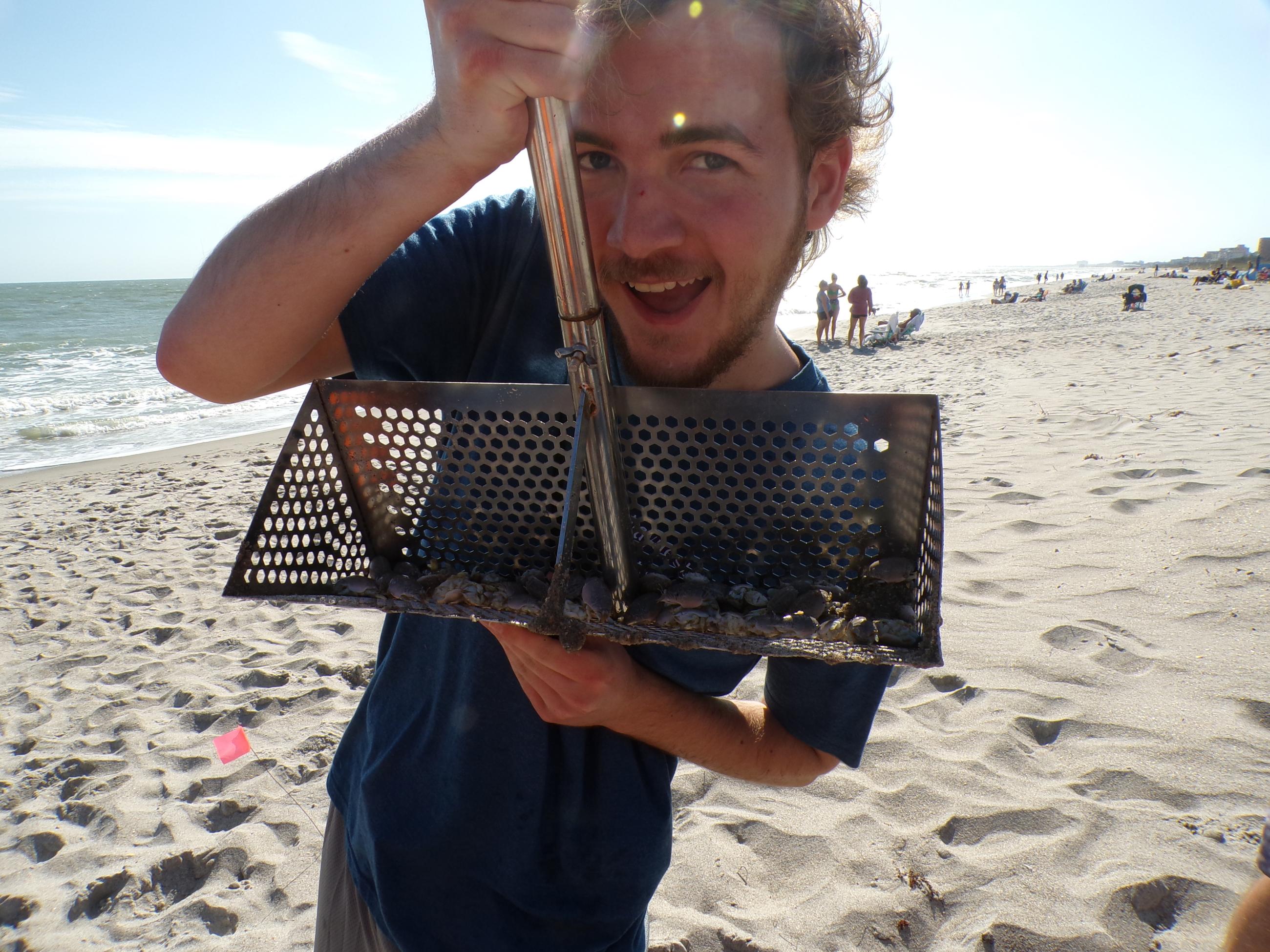 Student holding up rake on the beach