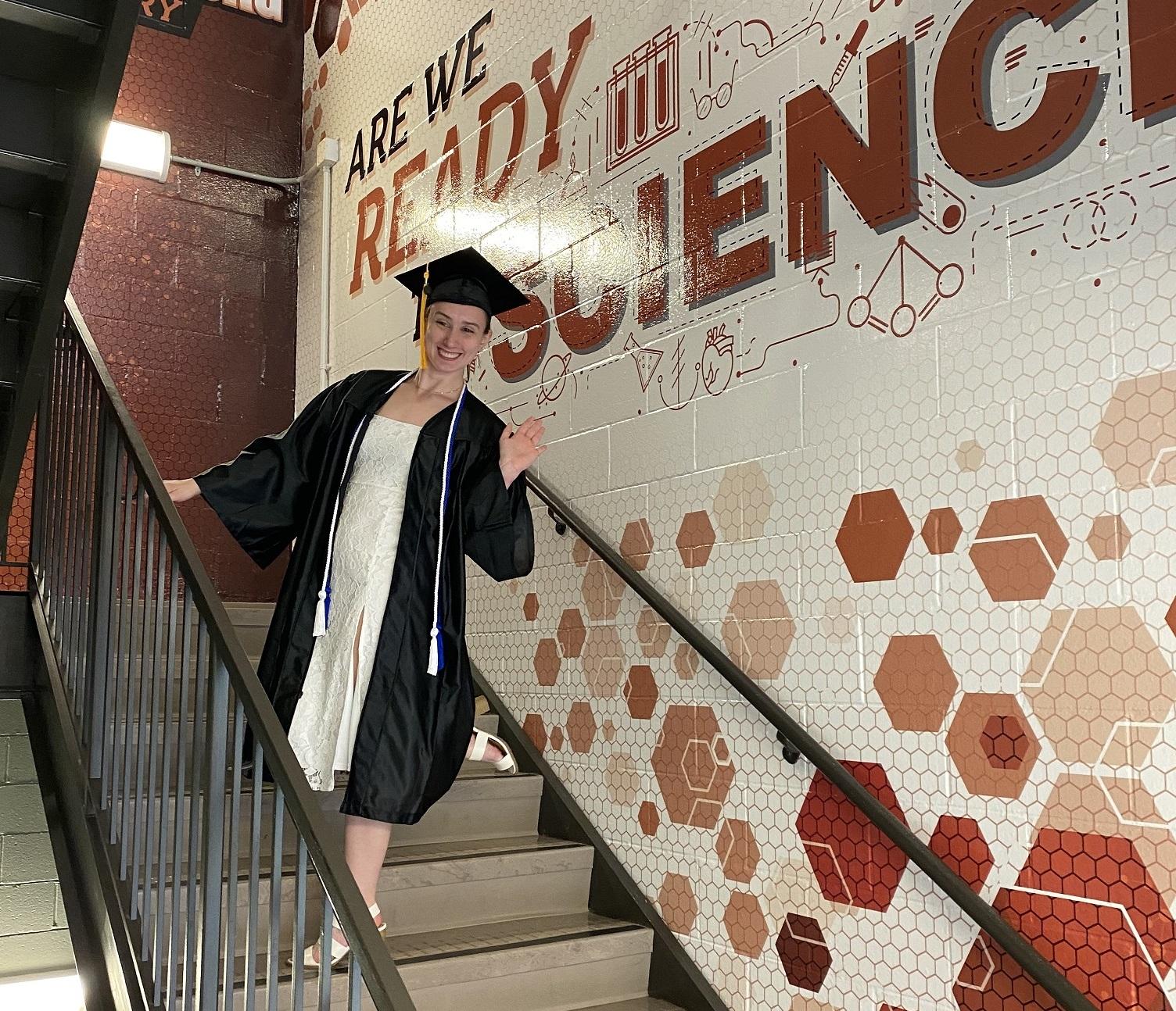 Kate James standing in a stairwell wearing academic regalia 